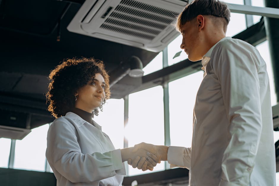 Business professionals exchange a handshake in a modern office setting, symbolizing collaboration.